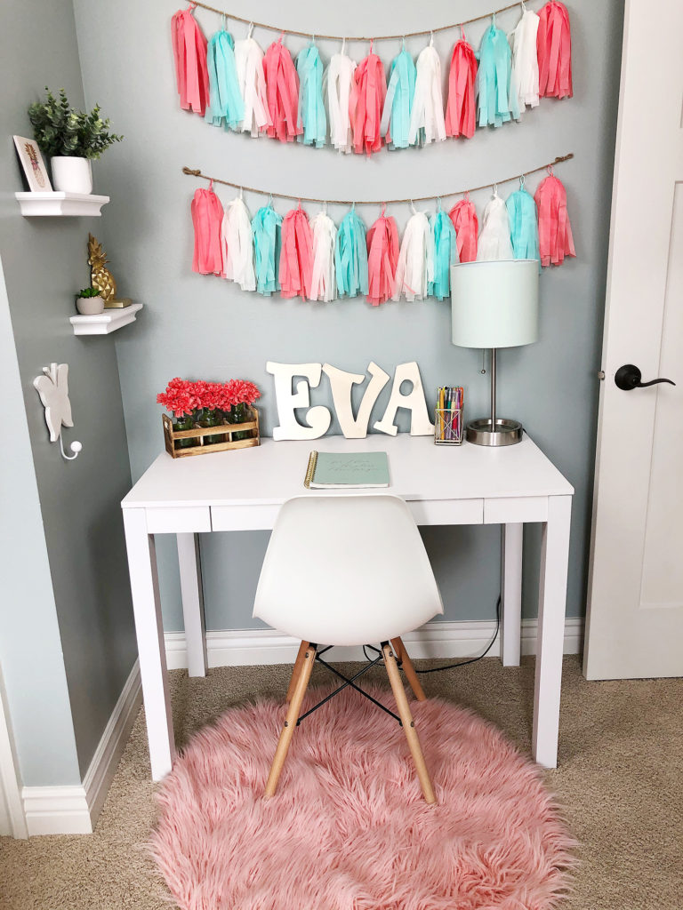 Girls white desk with teal lamp, pink rug and tassel garlands. 